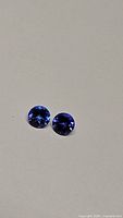 Two round cut deep purple blue tanzanite gemstones placed side by side to show size and color.