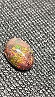 Close-up image of the oval cabochon Ethiopian black opal, showing its vibrant color play on a textured black background.