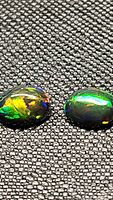 Close-up of two oval cabochon Ethiopian black opals on a textured black background showing vibrant rainbow color flashes.