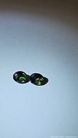 Pair of oval multicolored sapphires with green and blue shades photographed on white background.