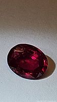Close-up photo of one side of the oval blood red ruby gemstone showing rich color and natural inclusions.
