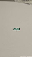 Two small rectangular emerald cut green gemstones on a white background, showing color and size.
