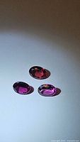 Three oval faceted fuchsia purple pink garnet gemstones arranged on a white background under natural light.
