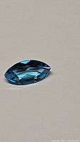 Single marquis cut blue topaz gemstone viewed from side angles showing facets and deep blue color.