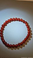 Fire red carnelian beaded bracelet arranged in circular form on neutral background, showing bright orange-red polished beads.