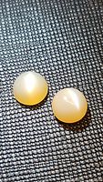 Two round cabochon peach moonstones with visible cat's eye effect placed on a textured black surface.