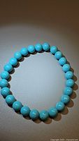 Photo of stretchy bracelet with round polished robin's egg blue turquoise beads approximately 8mm arranged in a circle on a surface.