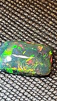 Close-up image of a rectangular black opal with intense vivid colors against a textured black background.