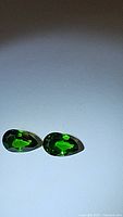 Two pear-shaped electric green Chrome Diopside gemstones displayed under lighting to show vivid color and clarity, placed on a white surface.