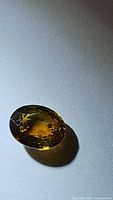 Close-up photo of the oval cut greenish yellow sphene gemstone showing clarity and color under direct light.
