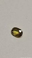 Oval shaped, yellow-green sphene gemstone with bright high luster on plain background.