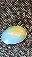 Oval natural Ethiopian opal on textured black background showing blue and green flashes.