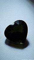 Heart shaped dark green tourmaline against a light background, showing color and general shape.