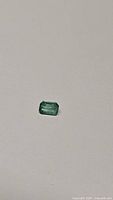 Top view showing rectangular emerald cut natural emerald with visible internal inclusions and vibrant green color on white background.