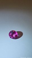 Photo of single oval natural hot pink topaz gemstone on a plain background showcasing color and cut.