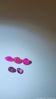Five natural rubies displayed on a plain background showing variation in hues from deep pink to red-purple and different shapes including marquise, oval, round, and pear cuts.