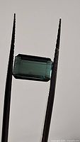 Clear close-up showing the rectangular emerald-cut natural paraiba blue tourmaline held by tweezers.