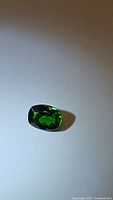 Photo of 1.25ct cushion cut green Russian chrome diopside gemstone on white background showing facets and clarity.