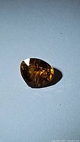 Faceted pear-shaped natural orange yellow tourmaline gemstone, viewed on a flat surface with light reflection showing clarity and inclusions.
