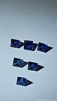 Six natural blue sapphire princess cut gemstones arranged on a flat surface, showing their clarity and color.