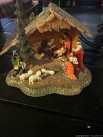 Front view showing entire nativity scene with stable, figures, and sheep on textured base with glitter roof.