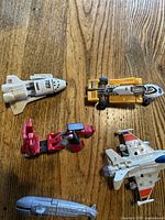 Top-down photo showing five 1980s GoBots toys including a white space shuttle, yellow racing vehicle, red transformable robot vehicle, gray submarine, and a fighter jet.