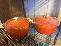 Two cast iron pots with lids on a metal rack under warm lighting, showing both pots side by side.