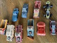 Top-down view of 11 toy vehicles including race cars, fire trucks, construction vehicles, and utility trucks on wood floor