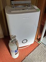 Frigidaire dehumidifier and Chubb fire extinguisher side by side on a carpeted floor near wood paneling.