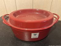 Red Doufeu cast iron enameled pot with lid and side handles on a black surface, showing the full pot.