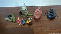Two green GI Joe MANTA sailboats, one with intact camouflage sail and mast, one with torn sail and missing mast, orange GI Joe Devilfish, blue Cobra Night Landing Raft, and three GI Joe action figures lined up