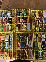 Top down view of multiple yellow trays filled with various Dinky car models including trucks, fire trucks, cars, and airplanes.