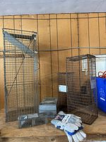 Overview photo showing all items in the lot on a wooden surface: three wire mesh traps, two metal box traps, and one pair of work gloves.