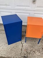 Photo showing the blue and orange metal storage cabinets side by side on concrete, closed.