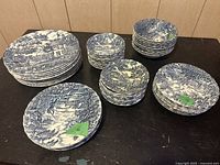 Overview of six stacks of blue and white plates and bowls on black surface against wood panel wall