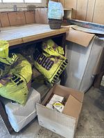 Photo of yellow bags labeled orchid bark, large bag of soil or peat moss, and a cardboard box with small items inside under a workbench.