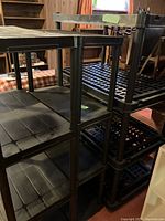 Three black plastic shelving units stacked together in a room, showing the various depths of the shelves and the overall structure.