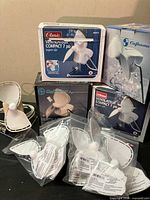 Five boxed portable table top fans with multiple replacement blades in plastic bags in front, showing branding and packaging.