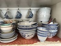 Wide view of stacked and nested bowls of various styles with hanging blue and white cups overhead.