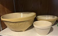Three mixing bowls displayed on shelf: one large yellow bowl, one medium yellow bowl, and one small white bowl.