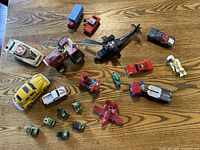 Top view of the entire lot showing all toy vehicles including cars, tractor, helicopter, military trucks, tanks, airplane, and astronaut figurine arranged on a wood surface.