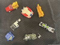 Top view of all eight toy vehicles laid out on a black fabric background, showing various types including crane, spaceship, tank, and police jeep.
