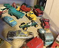 Overview of assorted vintage small toy vehicles including trucks, cars, and tractors on display surface