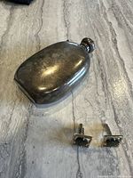 Photo showing tarnished vintage sterling silver perfume bottle pendant and a pair of cufflinks with dark stone inlays on a marble surface.