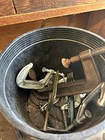 Photo of metal C-clamps and assorted screws in a black bucket