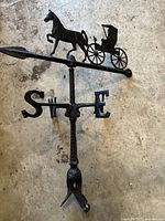 Top view of black metal weather vane with horse pulling carriage design on directional bar.