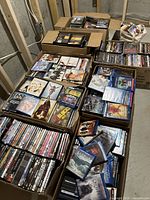 Wide shot showing multiple cardboard boxes filled with DVD and Blu-ray cases on concrete floor