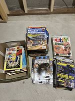 Overview photo showing four main stacks of vintage magazines including Model Railroader, Nintendo Power, GamePro, and a box filled with additional magazines including Arbie's Double Digest comics.