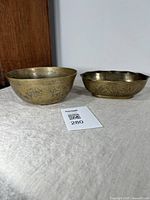 Photo showing two vintage brass bowls, one round and one oblong, with etched designs visible on their exterior surfaces.