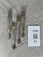 Four forks laid out on gray cloth next to lot number card